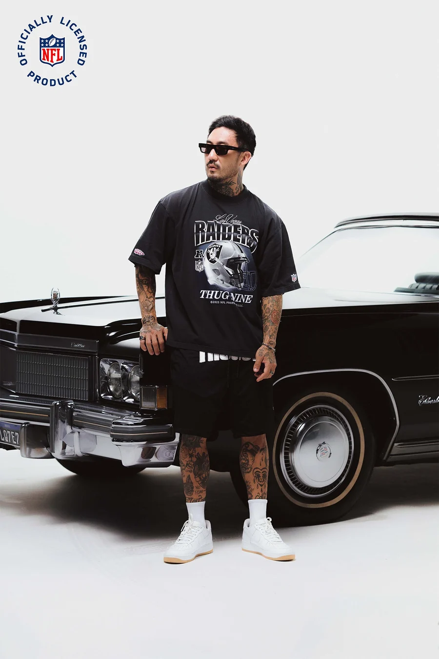 Modelo de camiseta Raiders e bermuda preta em frente a um Cadillac