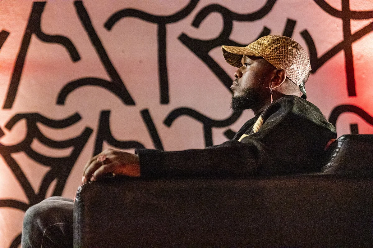 Djonga sentado em um sofá durante o lançamento do álbum O Dono do Lugar em 2022
