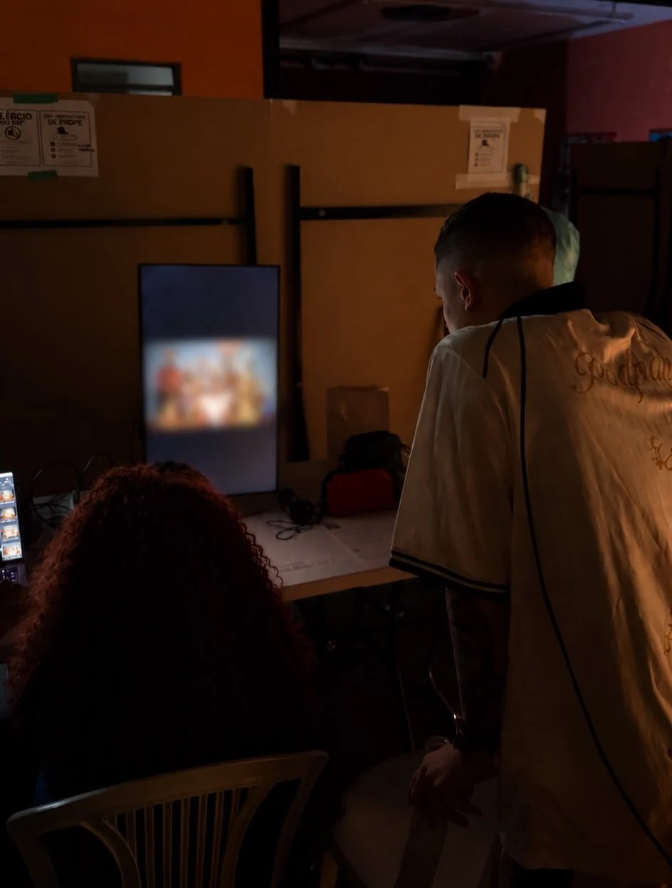 MC Hariel de costas, em estúdio, acompanhando a produção do novo projeto em frente a um monitor